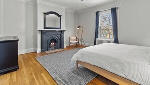 A bedroom with a fireplace, a bed, a chair, and a floor lamp. - Emerald Victorian Patio  4+1 Bd Parking (St. John's)