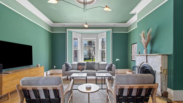 A living room with a green wall, a fireplace, a sofa, and a television. - Emerald Victorian Patio  4+1 Bd Parking (St. John's)