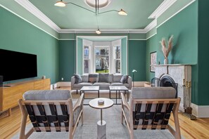 A living room with a green wall, a fireplace, a sofa, and a television. - Emerald Victorian Patio  4+1 Bd Parking (St. John's)