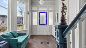 A hallway with a green sofa, a staircase, and a view through a door with a blue stained glass window. - Emerald Victorian Patio  4+1 Bd Parking (St. John's)