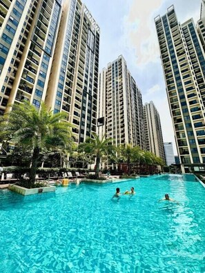 Una piscina rodeada de edificios residenciales altos, palmeras y sillas de descanso.