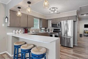 Una cocina moderna con una isla central, taburetes de bar, electrodomésticos de acero inoxidable e iluminación colgante.