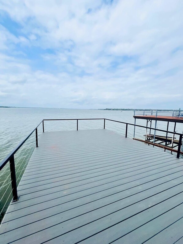 A wooden pier extending into calm water with a metal railing and a bench.