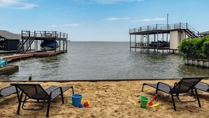 Uma praia com duas docas, uma área arenosa com espreguiçadeiras e uma vista clara da água.