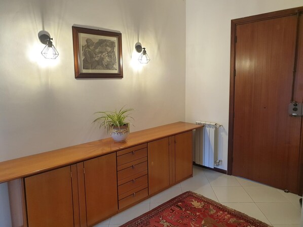 A hallway with a wooden cabinet, a potted plant, a framed picture, and a radiator.