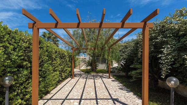 Una estructura de pérgola con un sendero de piedra que la atraviesa, rodeada de follaje.