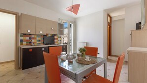 Una cocina moderna con un salpicadero colorido, un comedor con sillas naranjas y una pequeña mesa con una cafetera y frascos.