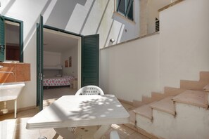 Ein kleiner, sonniger Raum mit einem Bett, einem Tisch und einem Stuhl. Eine Treppe führt zu einer oberen Ebene.