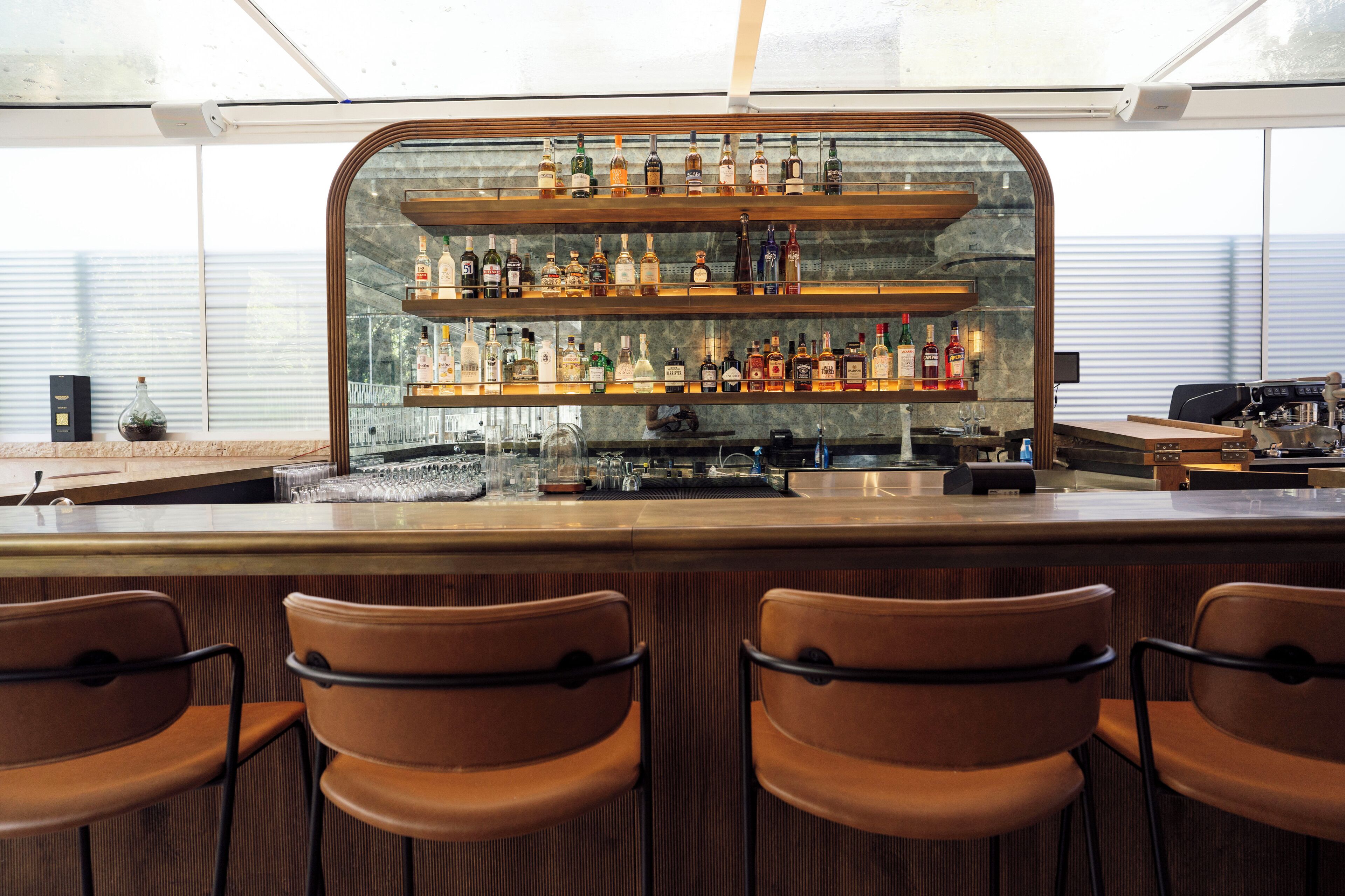 Zona de bar con una vitrina de botellas de licores, una barra y cuatro sillas marrones.