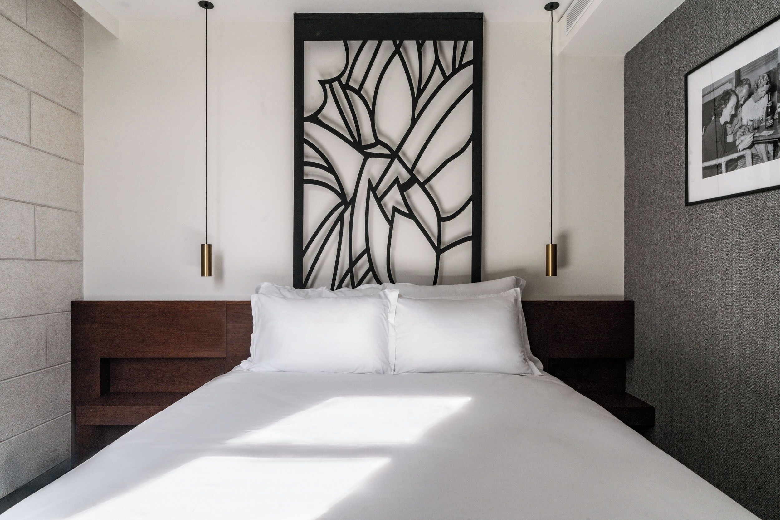 A modern hotel room with a large bed, a decorative wall panel, and a framed photo on the wall.