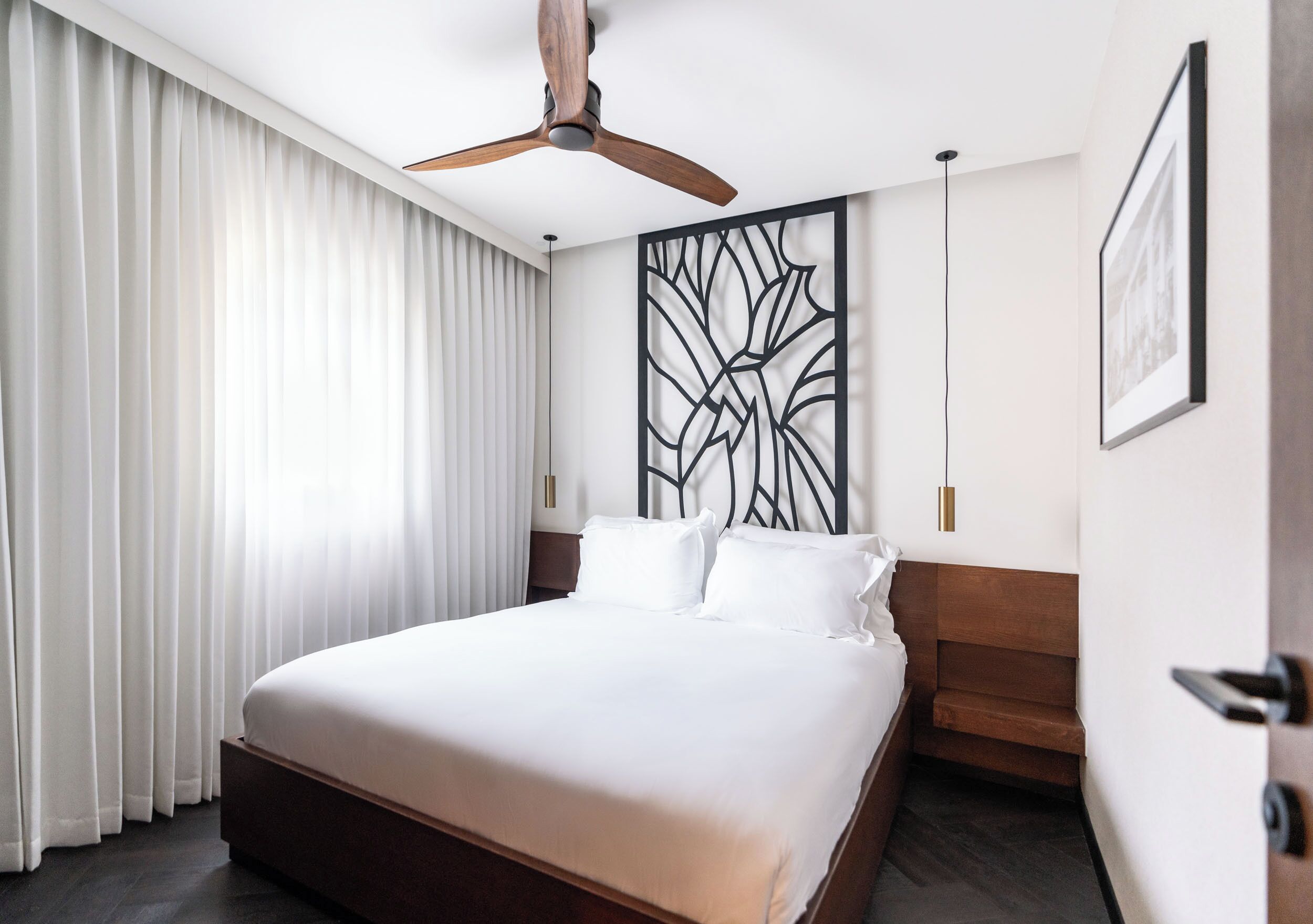 A hotel room with a large bed, a ceiling fan, a decorative wall panel, and a framed picture on the wall.