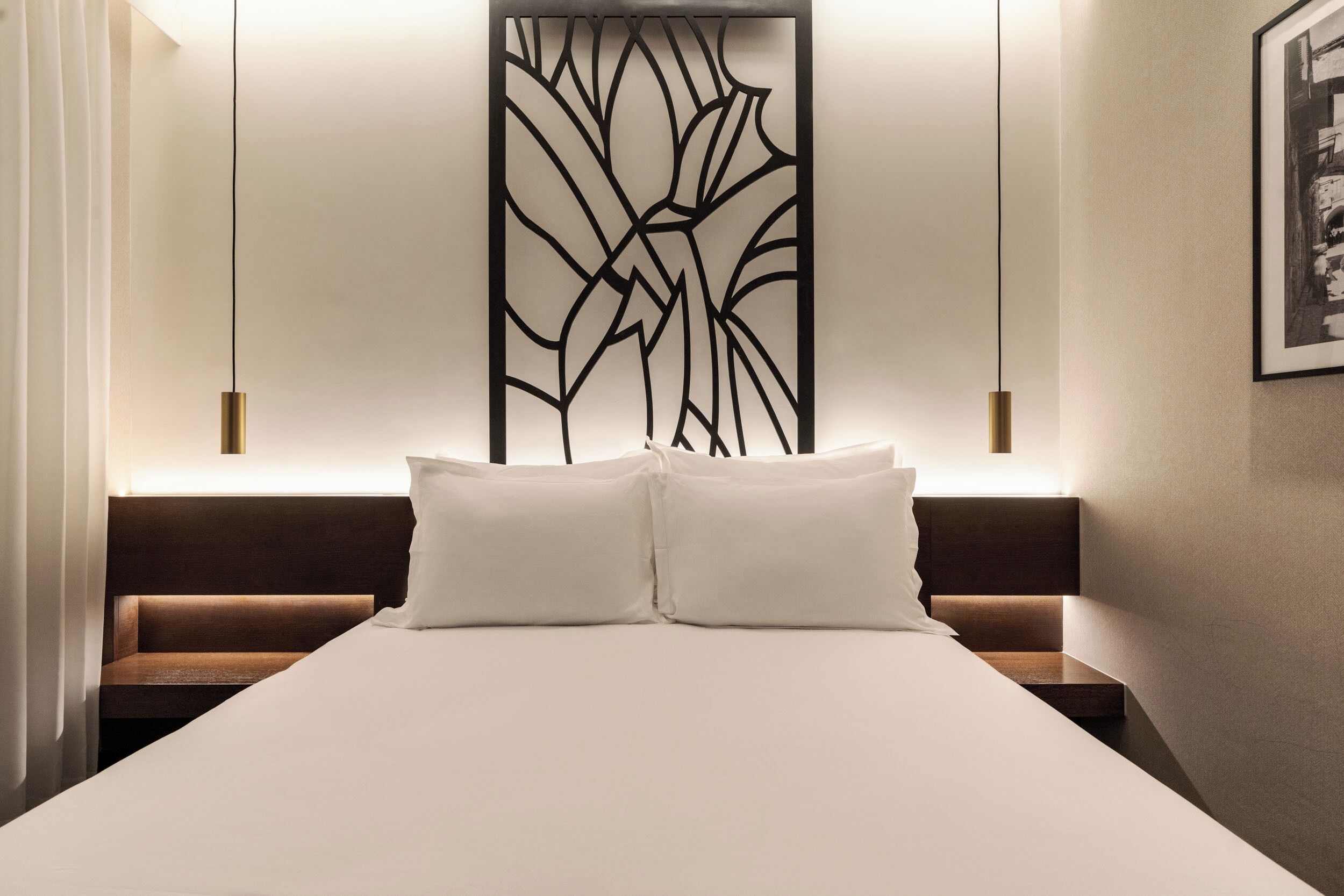 Une chambre d’hôtel moderne avec un grand lit, deux tables de chevet, un panneau décoratif au mur et un tableau encadré.