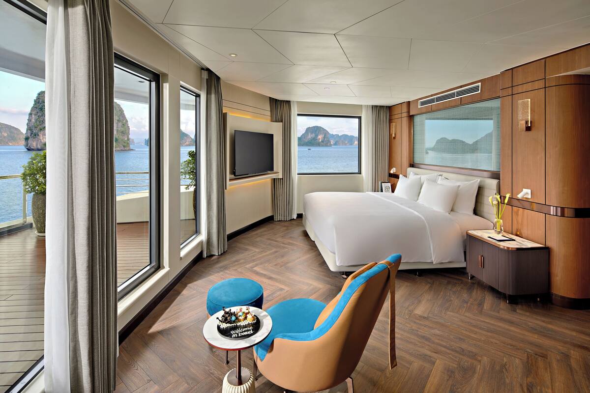 Ein modernes Hotelzimmer mit einem großen Bett, einem Fernseher, einem kleinen Tisch mit Kuchen und Blick aufs Meer.