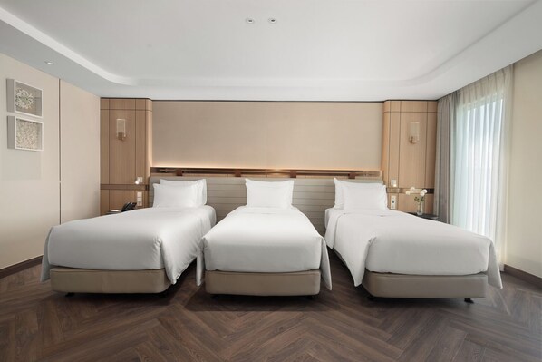 Habitación de hotel con tres camas, suelo de madera y diseño moderno.
