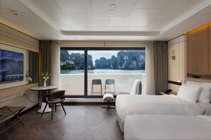Habitación de hotel con una cama grande, un escritorio con silla, una mesita con un florero y un televisor.