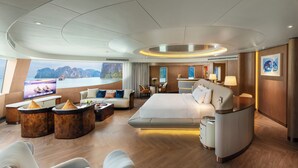 Une chambre d’hôtel moderne dotée d’un grand lit, d’un coin salon avec des canapés et une table basse, d’une télévision et d’une vue sur la mer.