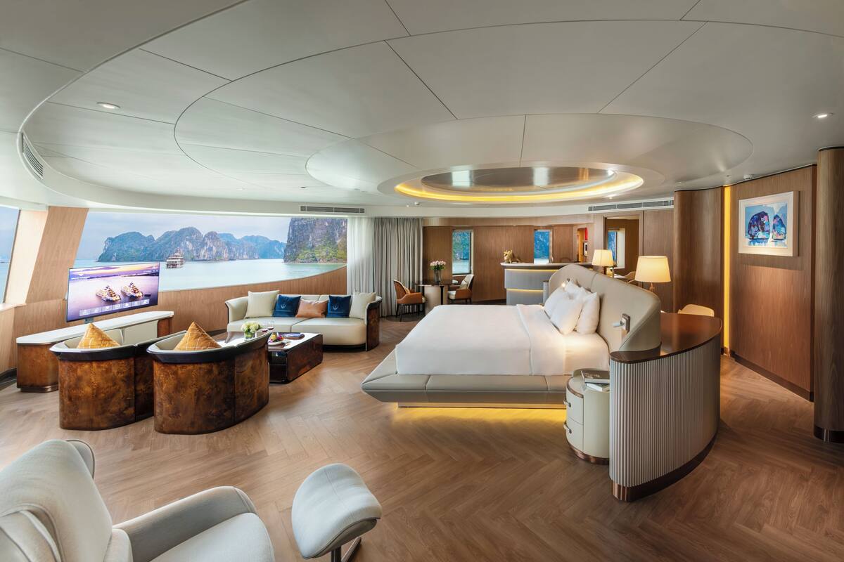 Ein modernes Hotelzimmer mit einem großen Bett, einer Sitzecke mit Sofas und einem Couchtisch, einem Fernseher und Blick auf das Meer.