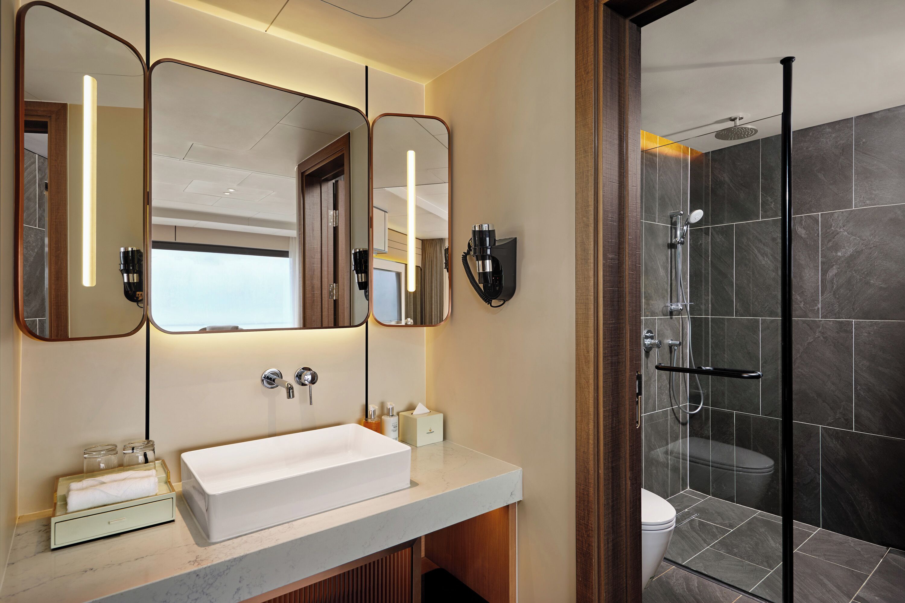 A modern bathroom with a large mirror, a white sink, and a glass-enclosed shower.