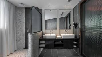 A modern bathroom with two sinks, a large mirror, and a shower area.
