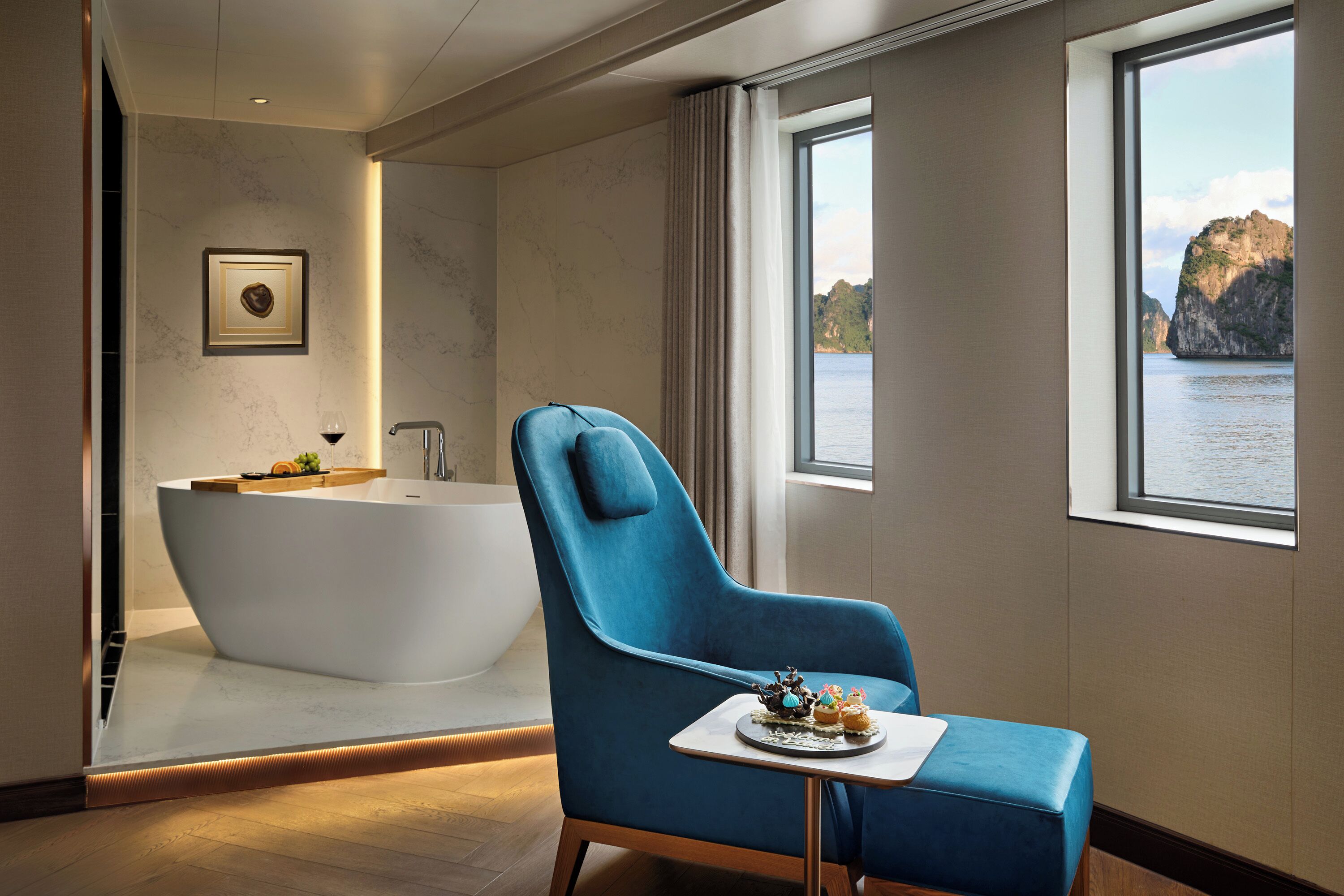 A modern bathroom with a bathtub, a blue chair, and a table with a dessert.