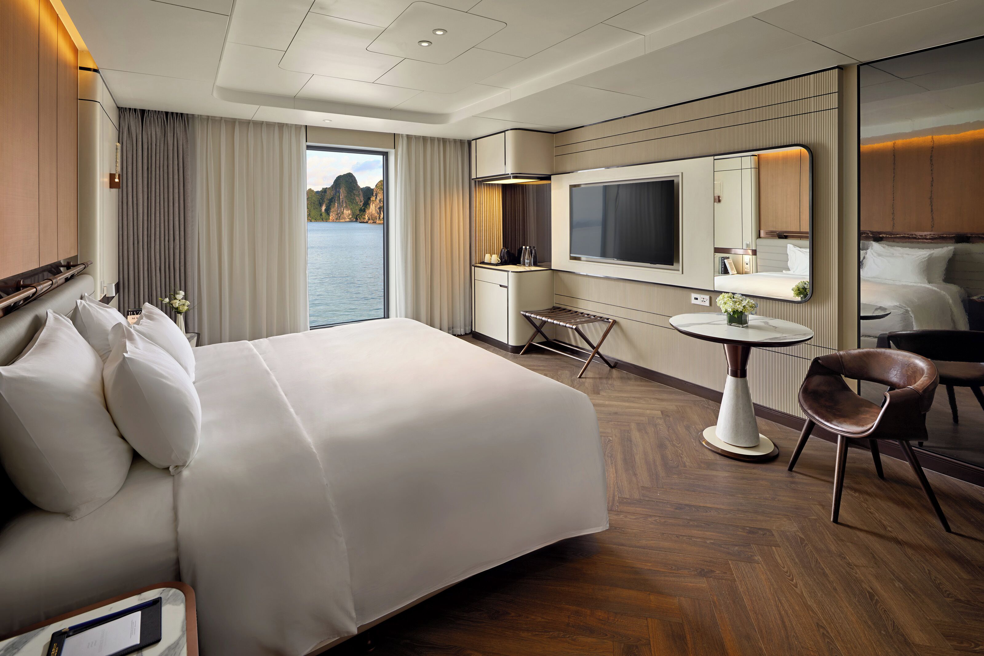 Habitación de hotel con una cama grande, un escritorio, una silla, una mesita, un televisor y vista al agua.