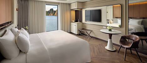 Habitación de hotel con una cama grande, un escritorio, una silla, una mesita, un televisor y vista al agua.