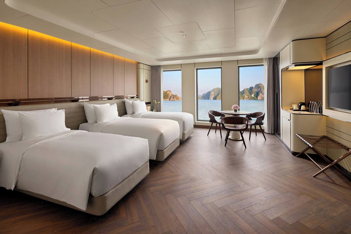 Ein Hotelzimmer mit zwei Betten, einem Essbereich und Blick auf das Meer.