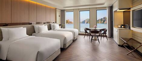 A hotel room with two beds, a dining area, and a view of the sea.