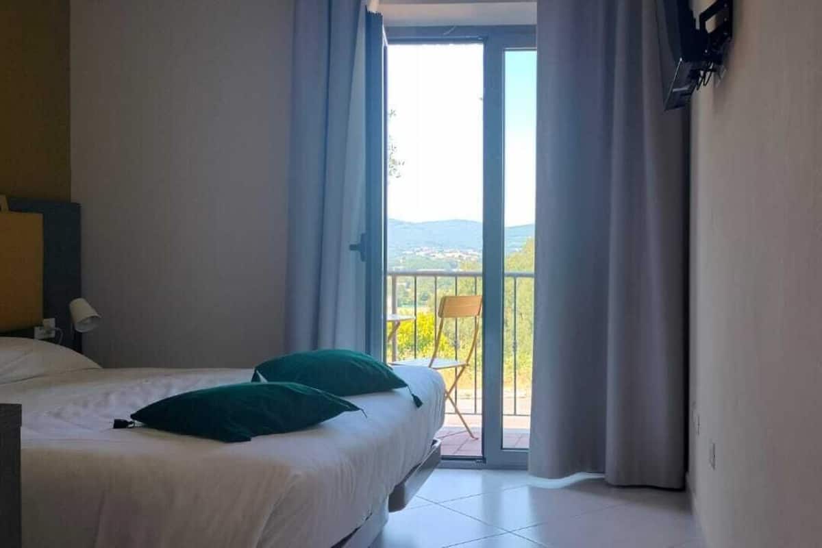 A hotel room with a bed, a chair, and a balcony with a view of the landscape.