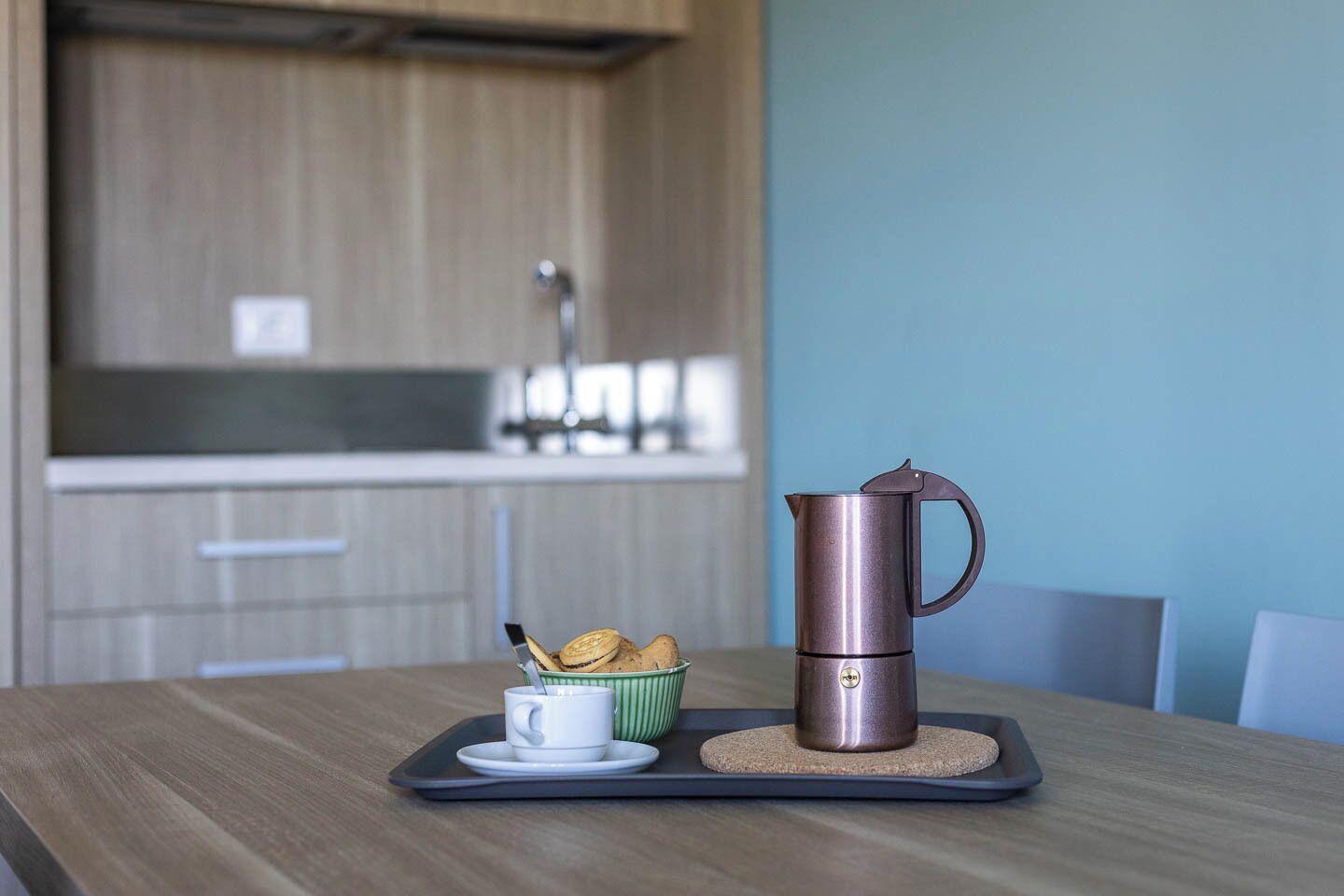A kitchen with a coffee maker on a tray, a cup, and a bowl of cookies.