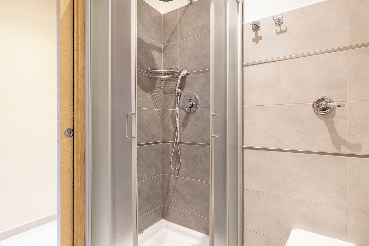 Eine Dusche mit Glaswand, Handbrause und am Wand montiertem Wasserhahn.