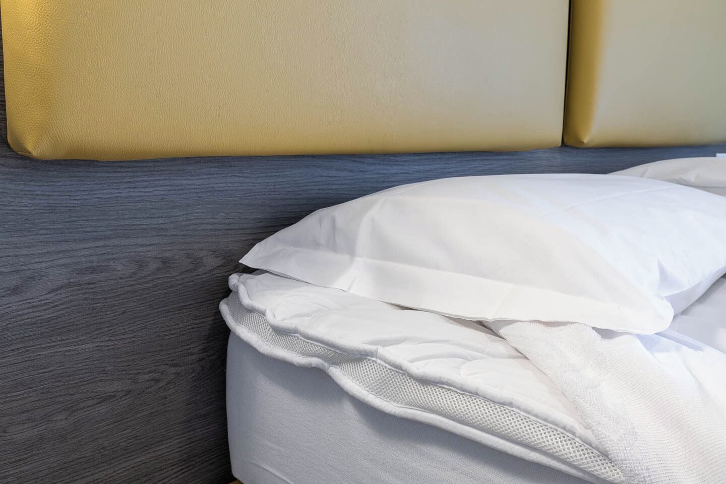 Uma cama com roupa de cama branca e cabeceira cinzenta.