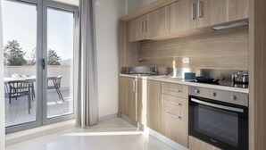 Una cucina moderna con mobili in legno, forno integrato e una porta vetrata scorrevole che dà su un balcone con arredi da esterno.