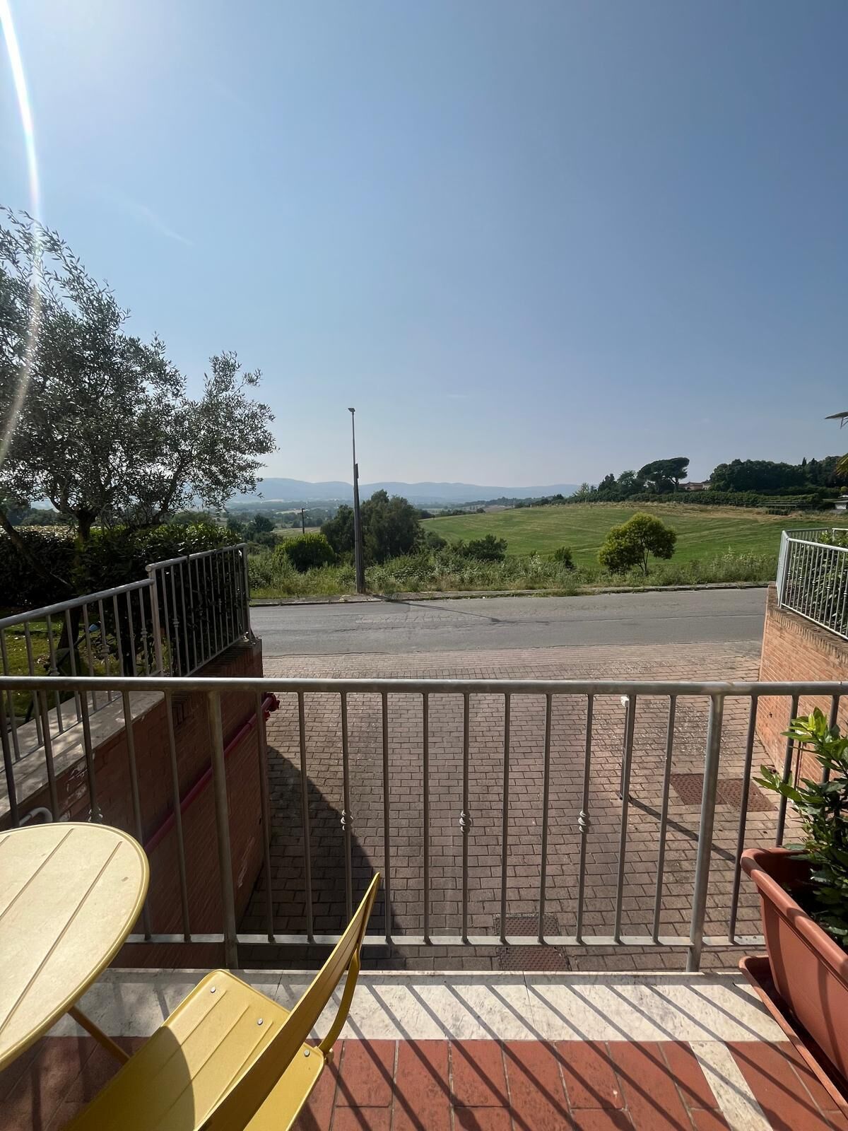 Uma varanda com vista para uma área pavimentada e colinas ao longe.