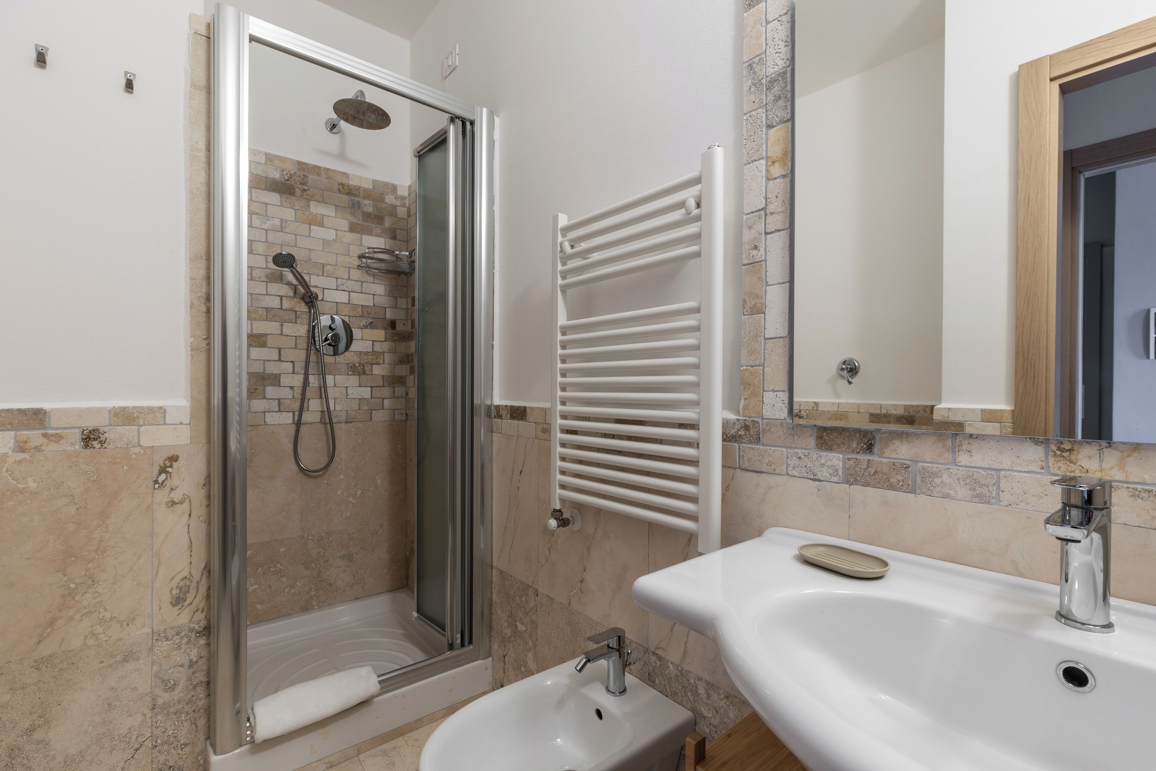 Un baño con ducha, lavamanos y un perchero para toallas.