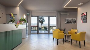 Un'area reception di un hotel con un bancone verde, sedie gialle e un balcone con vista.