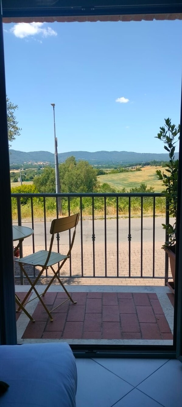 A balcony with a view of a rural landscape, a metal chair, a small table, and a potted plant. - Tuscasì Aparthotel (Sovicille)