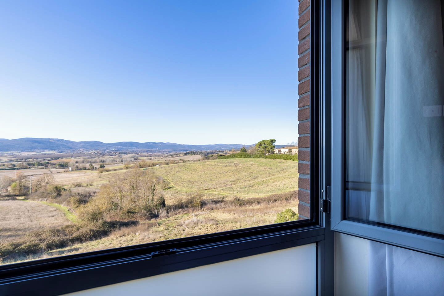 A window with a view of a rural landscape, including fields and distant hills.