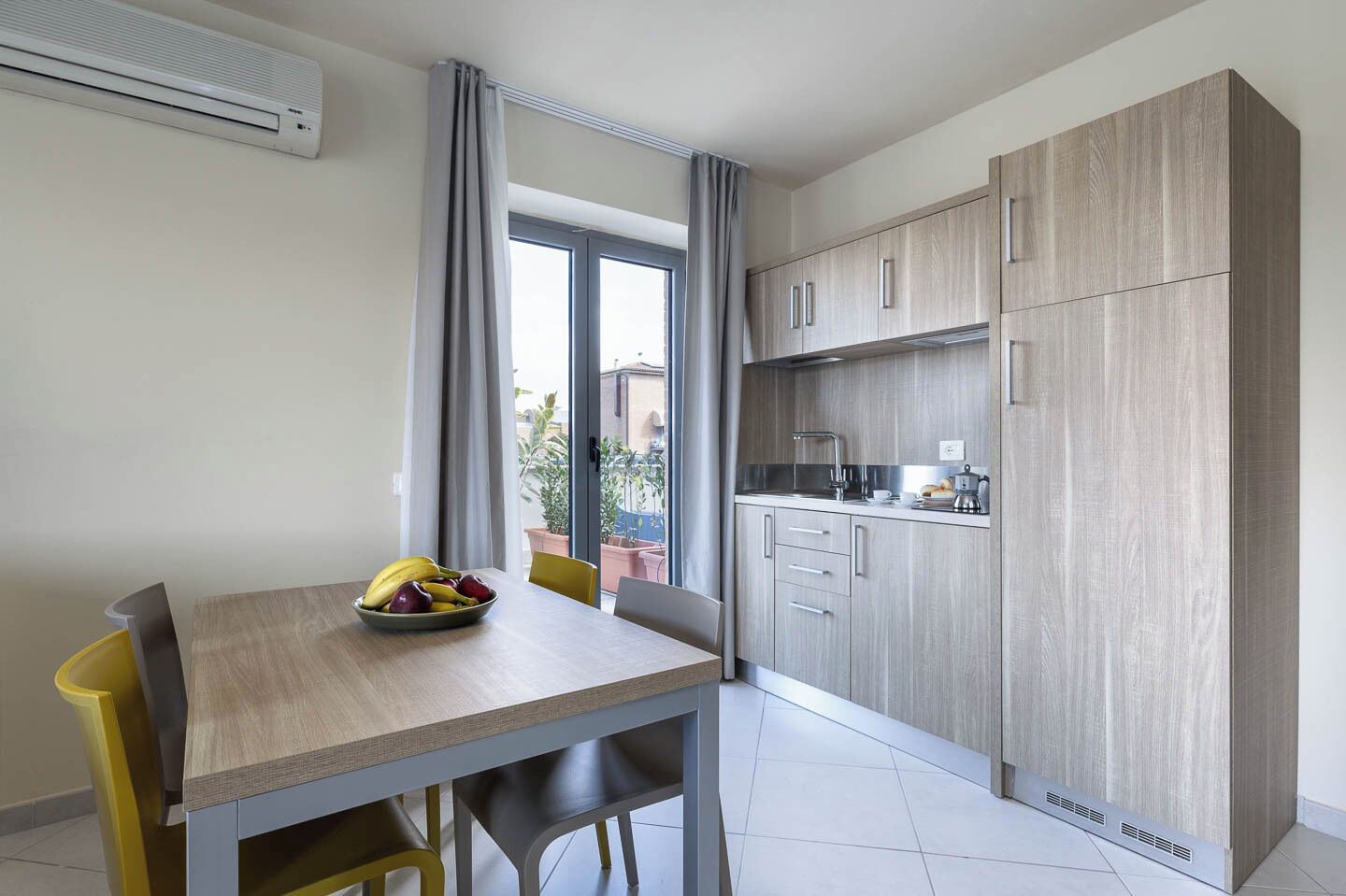 A modern kitchen with wooden cabinets, a built-in oven, and a window overlooking a garden.