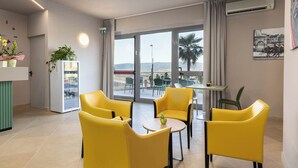 Una camera d'albergo moderna con sedie gialle, un tavolino, un frigorifero e un balcone con vista sulla città e sulle montagne.