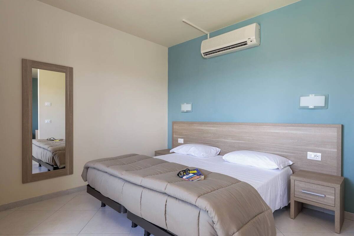 A bedroom with a bed, a nightstand, a mirror, and an air conditioning unit.