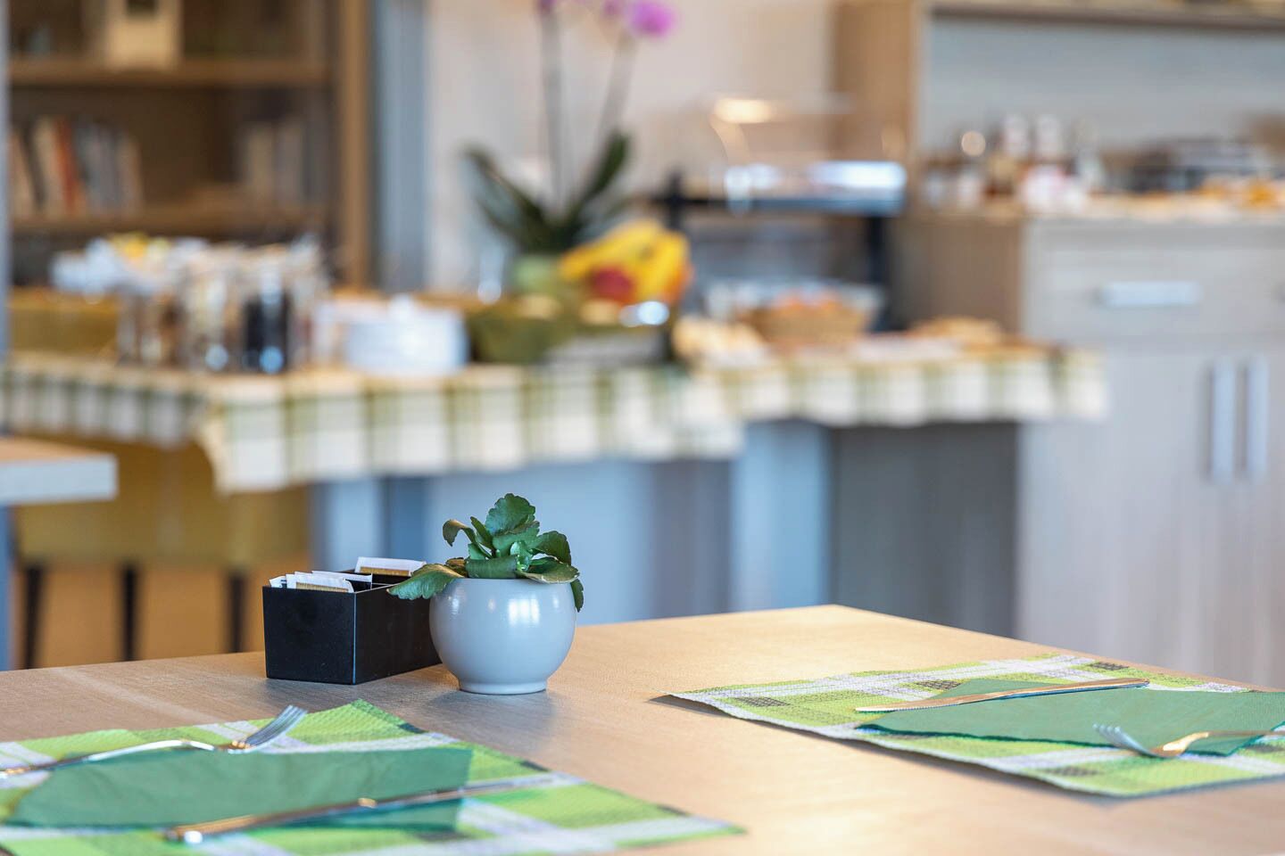 A kitchen with a table set for dining, a potted plant, and a checkered tablecloth.