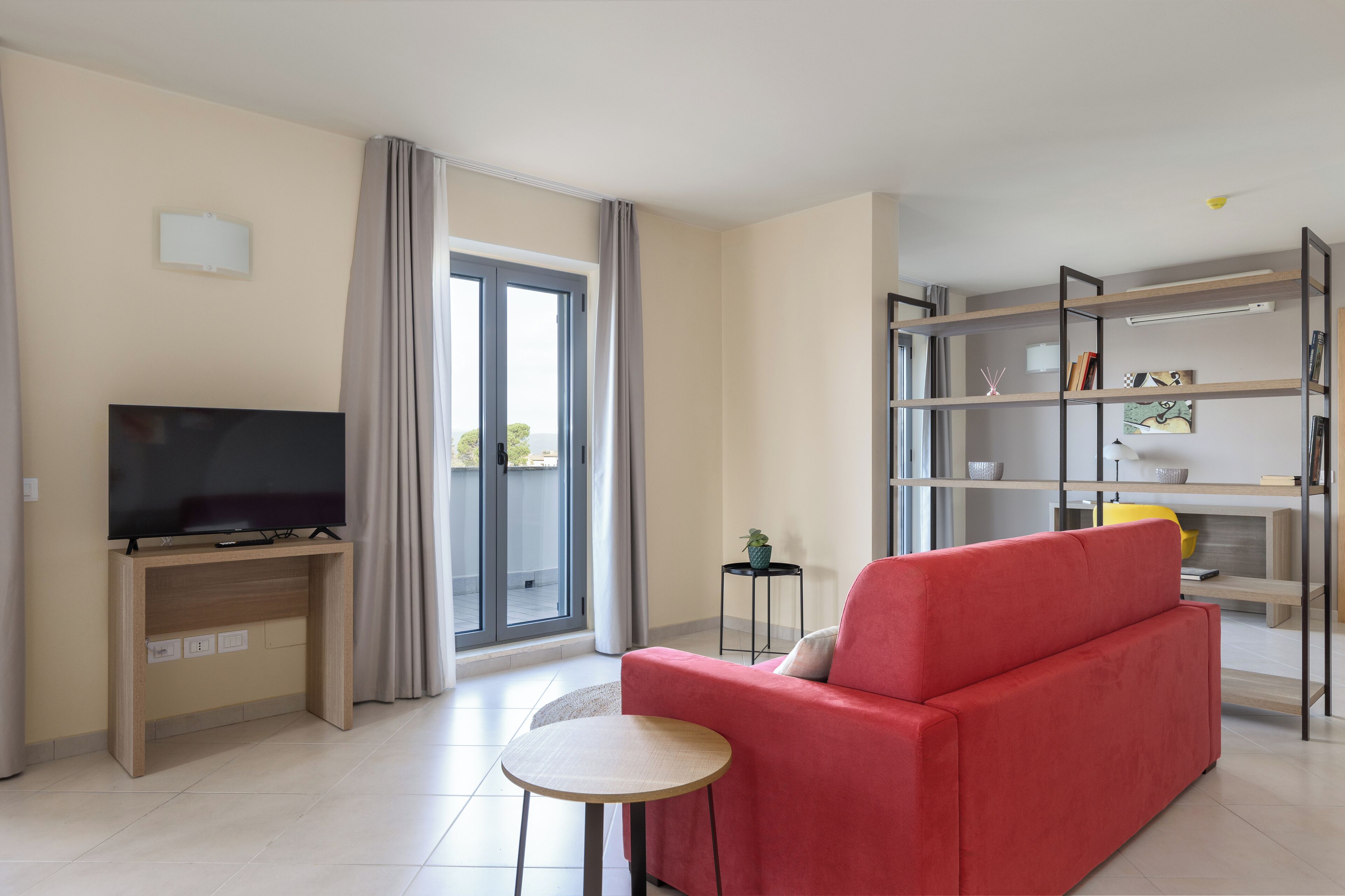 A modern living room with a red sofa, a TV on a wooden stand, a small table, and a bookshelf.