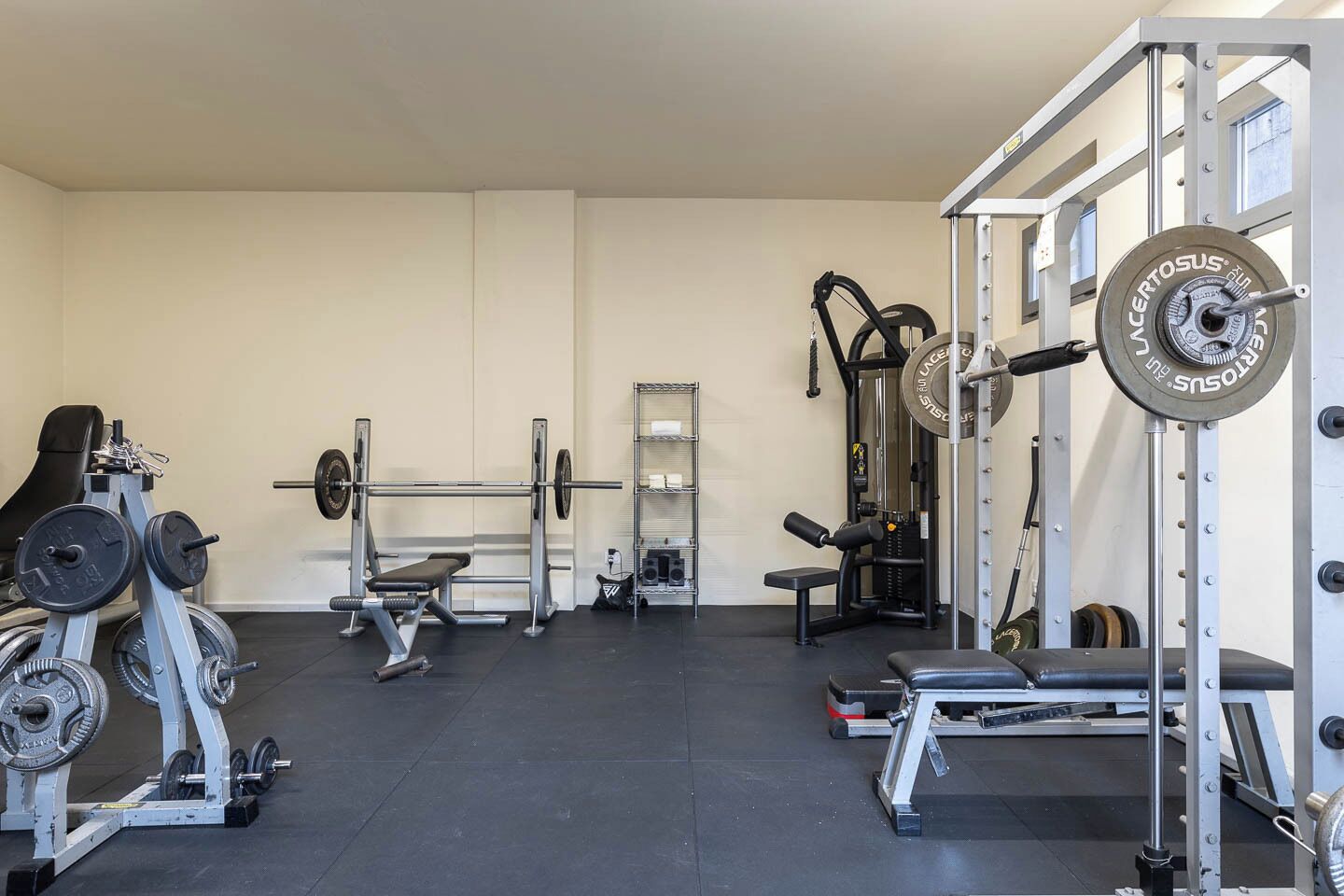 Un gimnasio con equipo de levantamiento de pesas, bancos y una jaula para sentadillas.