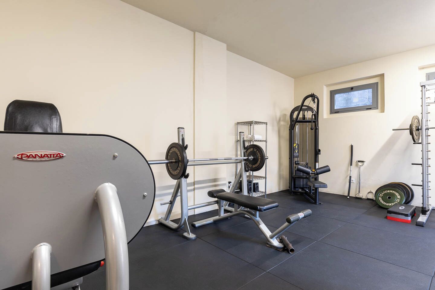 Een sportschool met gewichthefapparatuur, een bank en een power rack.