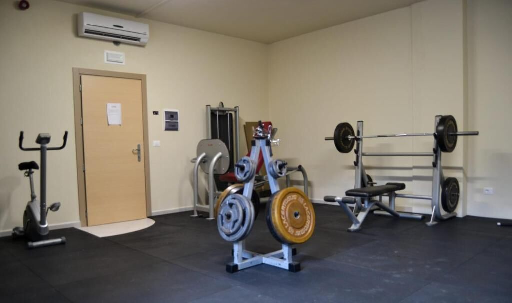 A gym with exercise equipment including a bench press, squat rack, and a stationary bike.