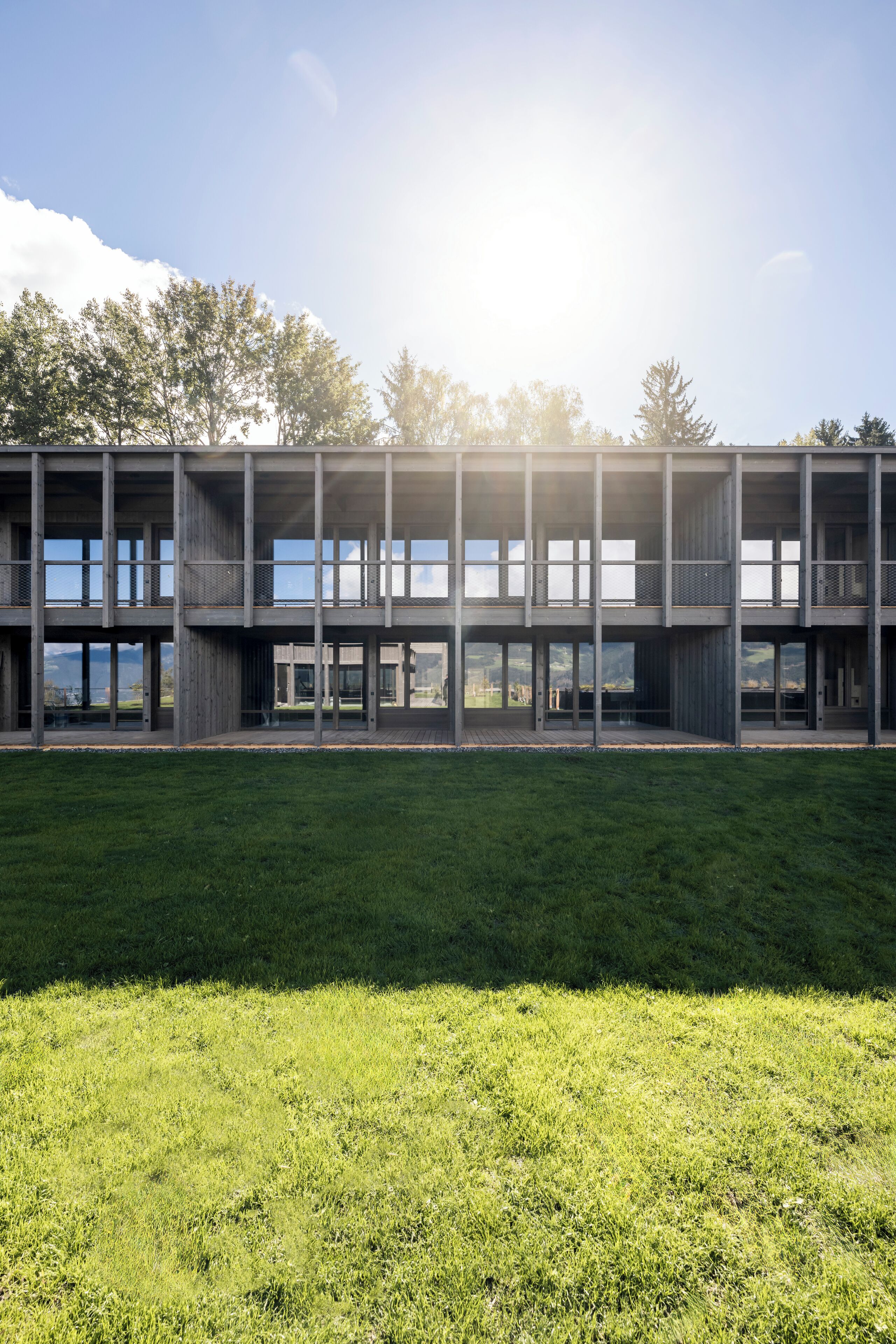 En modern byggnad med flera våningar och stora fönster, omgiven av en gräsyta.