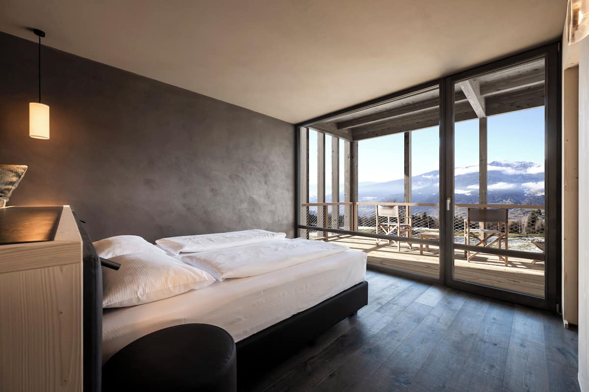 A modern bedroom with a large bed, a view of the outdoors, and a balcony with seating.
