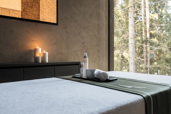 Un lit bien fait, avec une petite table de chevet sur laquelle on a disposé une tablette contenant des articles de toilette, une serviette et des bougies.