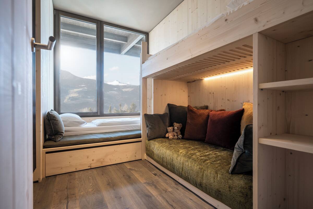 A cozy room with a built-in bed, a window with a view of mountains, and a wooden floor.